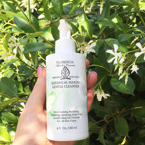 Hand holding a Botanical Marine Gentle Cleanser with greenery in the background.