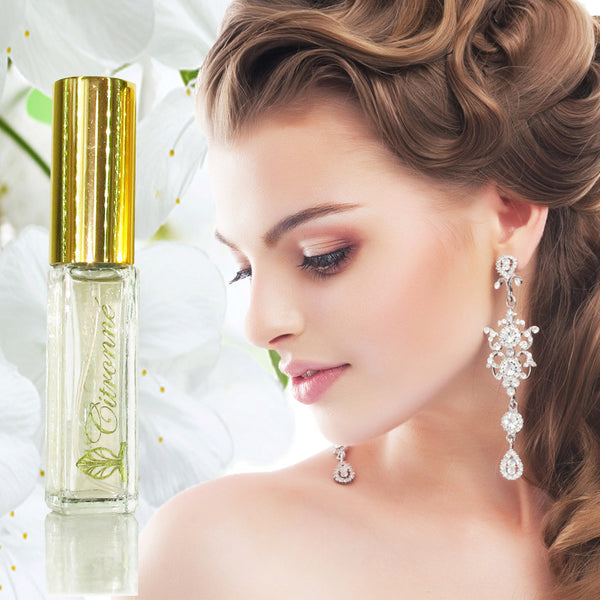 A small spray bottle of Citronné Fragrance in a clear bottle with gold top. Profile of a woman looking down with her hair half up and long shiny earrings. 