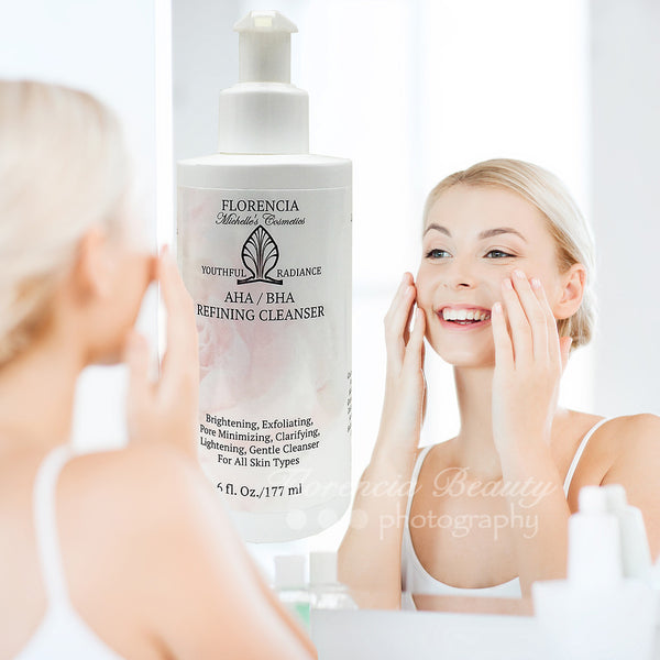 Woman with her hands on her cheeks looking into the mirror, washing her face with a bottle of AHA / BHA Refining Cleanser