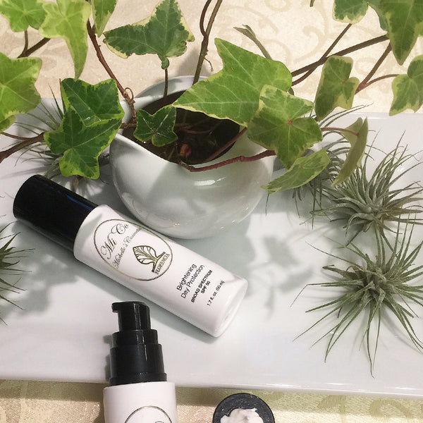 Two bottles of SPF 50 Brightening Day Protection Broad Spectrum next to a plant.