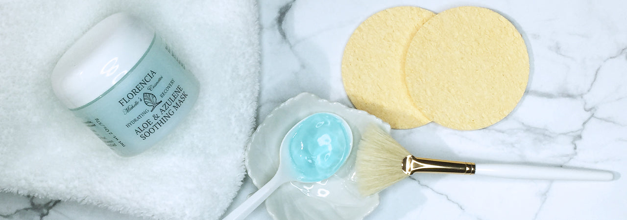 Jar of Aloe & Azulene Soothing mask resting on a white towel resting next to a spoon filled with the blue mask on a white dish.
